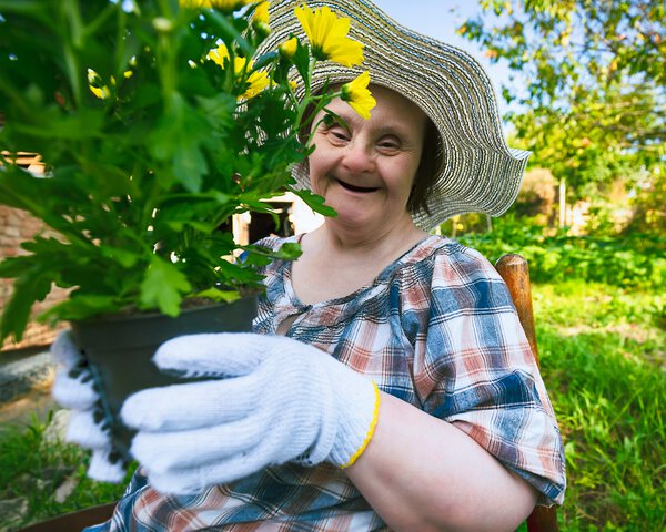 Eine ältere Frau mit Sonnenhut und Behinderung hält eine Pflanze in der Hand und lacht | © portishead1 - Getty Images