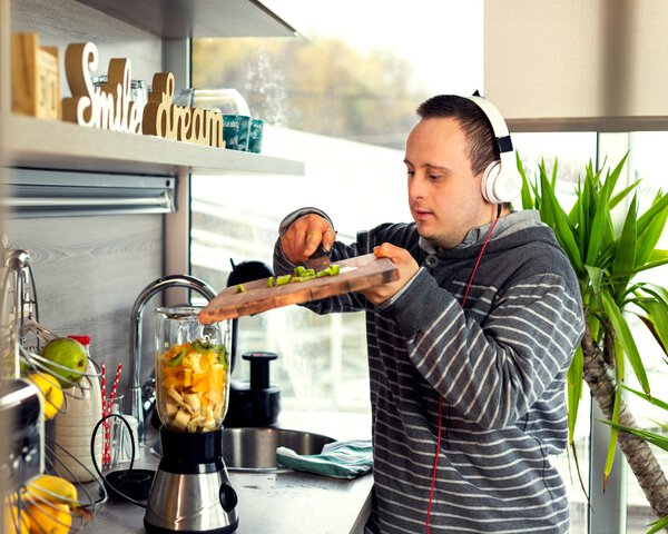 Ein Mann mit Kopfhörer und Behinderung gibt Früchte/Obst in einen Mixer | © Sladic - Getty Images